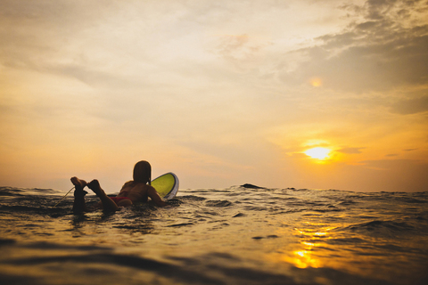 Frau auf Surfbrett im Meer liegend bei Sonnenuntergang, lizenzfreies Stockfoto
