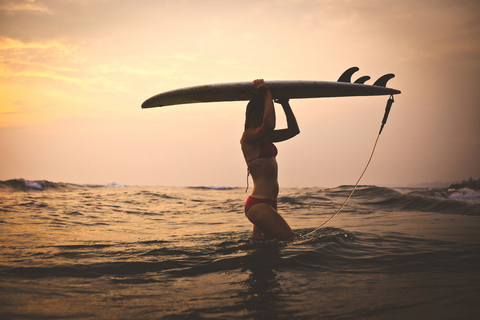 Frau trägt Surfbrett beim Spaziergang im Meer gegen den Himmel, lizenzfreies Stockfoto