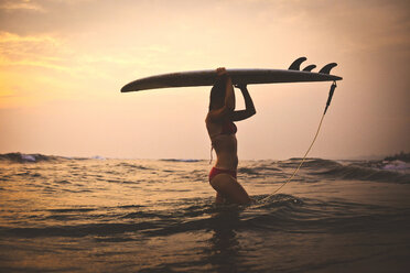 Woman carrying surfboard while walking in sea against sky - CAVF26774