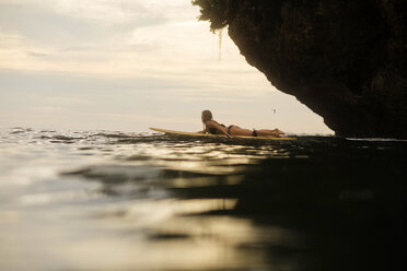 Seitenansicht einer Frau, die bei Sonnenuntergang im Meer surft - CAVF26790