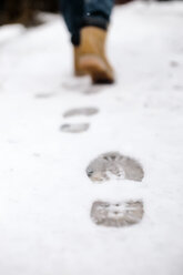 Tiefschnitt einer Frau, die auf einem schneebedeckten Gehweg Fußspuren hinterlässt - CAVF26796