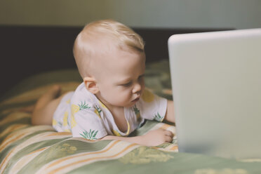 Nettes Baby mit Laptop-Computer auf dem Bett liegend zu Hause - CAVF26812