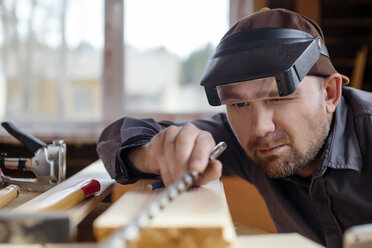 Carpenter wearing protective eyewear working at workbench in workshop - CAVF26821