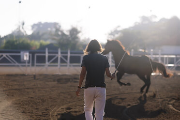 Rückansicht einer Frau, die ein Pferd auf einer Ranch trainiert - CAVF26830