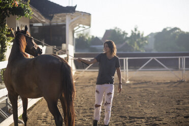 Frau berührt Pferd mit Tierpflegeausrüstung, während sie auf einer Ranch steht - CAVF26831
