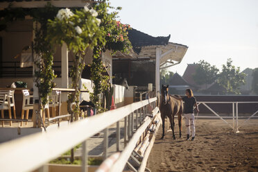 Frau in voller Länge, die ein Pferd streichelt, während sie auf einer Ranch steht - CAVF26833