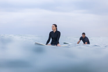 Friends sitting on surfboard in sea against sky - CAVF26844