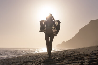 Frau in voller Länge im Bikini und mit Textil in der Hand gegen den klaren Himmel am Strand bei Sonnenuntergang - CAVF26865