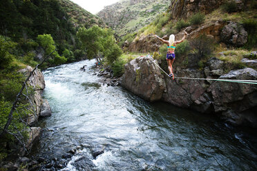 Rückansicht einer Frau, die sich auf einer Slackline über einen Fluss gegen Berge schwingt - CAVF26874