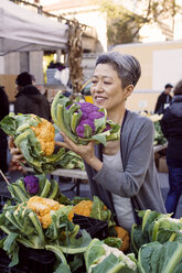 Lächelnde reife Frau beim Aussuchen von Blumenkohl auf dem Bauernmarkt - CAVF26889