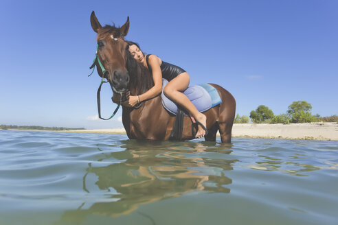 Indonesia, Bali, Woman lying on horse, in water - KNTF01106