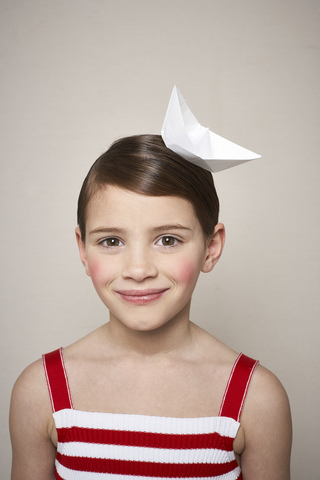 Porträt eines lächelnden kleinen Mädchens mit Papierschiffchen auf dem Kopf, lizenzfreies Stockfoto