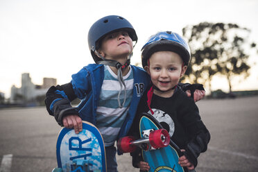 Portrait of cute boys standing with skateboard at field against clear sky - CAVF26930