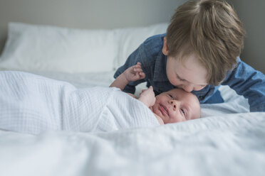 Boy kissing brother's forehead on bed at home - CAVF26936