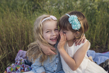 High angle view of girl whispering in sister's ear while sitting on blanket in park - CAVF26942