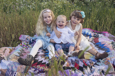 Porträt von glücklichen Schwestern, die auf einer Decke im Park sitzen - CAVF26944