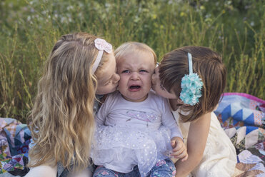 Mädchen küssen weinende Schwester, während sie auf einer Decke im Park sitzen - CAVF26945