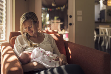 Mutter betrachtet ihre neugeborene Tochter, während sie sich auf einem Stuhl zu Hause entspannt - CAVF26953