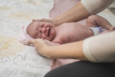 Cropped hands of mother holding crying newborn daughter on bed - CAVF26954