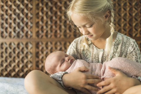 Schwester betrachtet neugeborenes Baby, während sie es auf dem Bett trägt, lizenzfreies Stockfoto