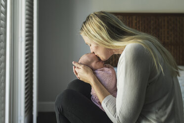 Seitenansicht einer Mutter, die ihre neugeborene Tochter küsst, während sie sie zu Hause trägt - CAVF26969