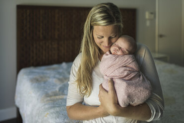 Mutter trägt ihre neugeborene Tochter im Sitzen auf dem Bett - CAVF26971