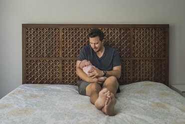 Vater trägt seine neugeborene Tochter im Sitzen auf dem Bett - CAVF26972