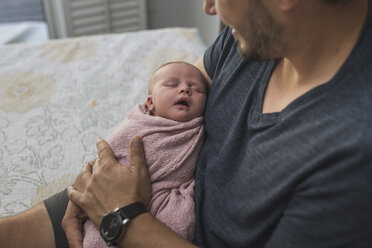 Ausgeschnittenes Bild eines Vaters, der seine neugeborene Tochter auf dem Bett sitzend trägt - CAVF26973