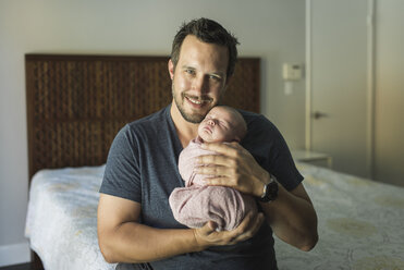 Porträt eines glücklichen Vaters, der seine neugeborene Tochter im Schlafzimmer trägt - CAVF26978