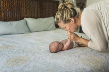 Mother kissing newborn daughter lying on bed - CAVF26989