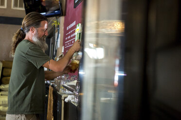 Seitenansicht eines Barkeepers, der Bier aus dem Zapfhahn einschenkt - CAVF27046