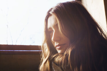 Thoughtful woman sitting by window on sunny day - CAVF27056