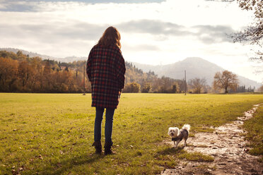 Rückansicht von Frau und Hund auf einer Wiese vor dem Himmel - CAVF27058