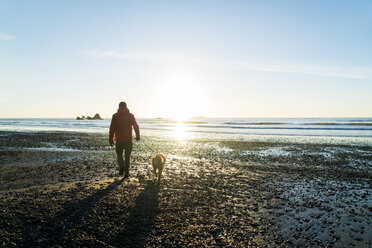 Rear view of hiker with Golden Retriever walking at Ruby beach against sky - CAVF27112