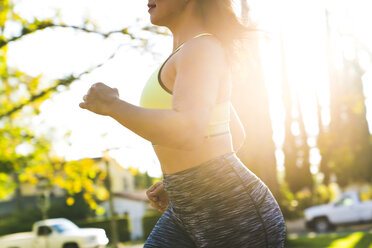 Mittelteil einer Frau beim Joggen im Park an einem sonnigen Tag - CAVF27120