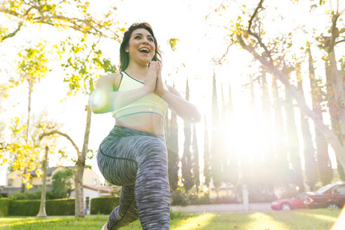 Low angle view of cheerful woman practicing yoga while exercising in park during sunny day - CAVF27132