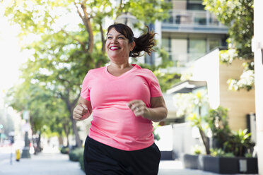 Fröhliche Frau beim Joggen auf dem Fußweg in der Stadt - CAVF27140