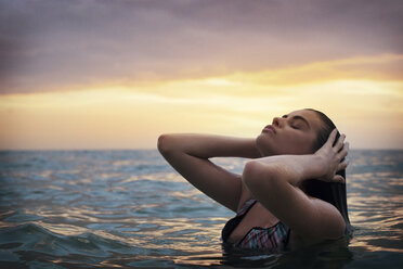Nahaufnahme einer jungen Frau, die sich bei Sonnenuntergang am Meer am Himmel erfreut - CAVF27141