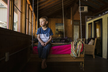 Thoughtful boy sitting on swing at home - CAVF27165