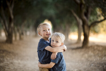 Porträt von Jungen, die sich umarmen, während sie auf einem Gehweg inmitten von Bäumen stehen - CAVF27168