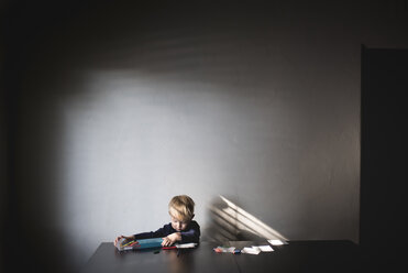 Junge nimmt Buntstifte aus der Schachtel, während er an einem Tisch an der Wand sitzt - CAVF27177
