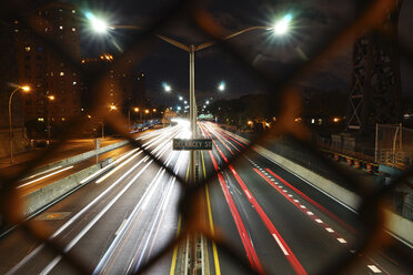 Lichtspuren auf der Stadtstraße durch den Zaun gesehen - CAVF27219