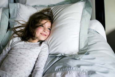 Smiling girl looking away while lying on bed at home - CAVF27241