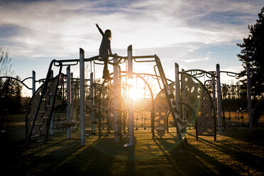 Mädchen spielt auf Metallstruktur im Park gegen bewölkten Himmel - CAVF27245