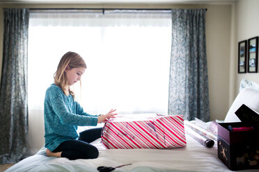 Seitenansicht eines Mädchens, das auf dem Bett kniend einen Geschenkkarton verpackt - CAVF27265