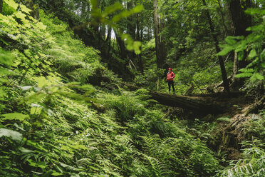 Frau mit Händen in den Taschen steht auf einem Baumstamm im Wald - CAVF27281