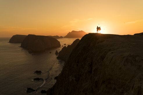Silhouette Paar steht auf Felsformation am Meer bei Sonnenuntergang - CAVF27309