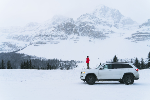 Side view of hiker standing on snow covered field by off-road vehicle during winter stock photo