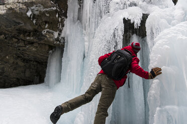 Rückansicht eines Mannes mit Rucksack, der an einem gefrorenen Wasserfall über einem Berg steht - CAVF27342