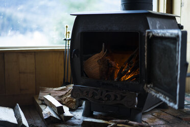 Close-up of wood burning stove by window on hardwood floor in cottage - CAVF27352